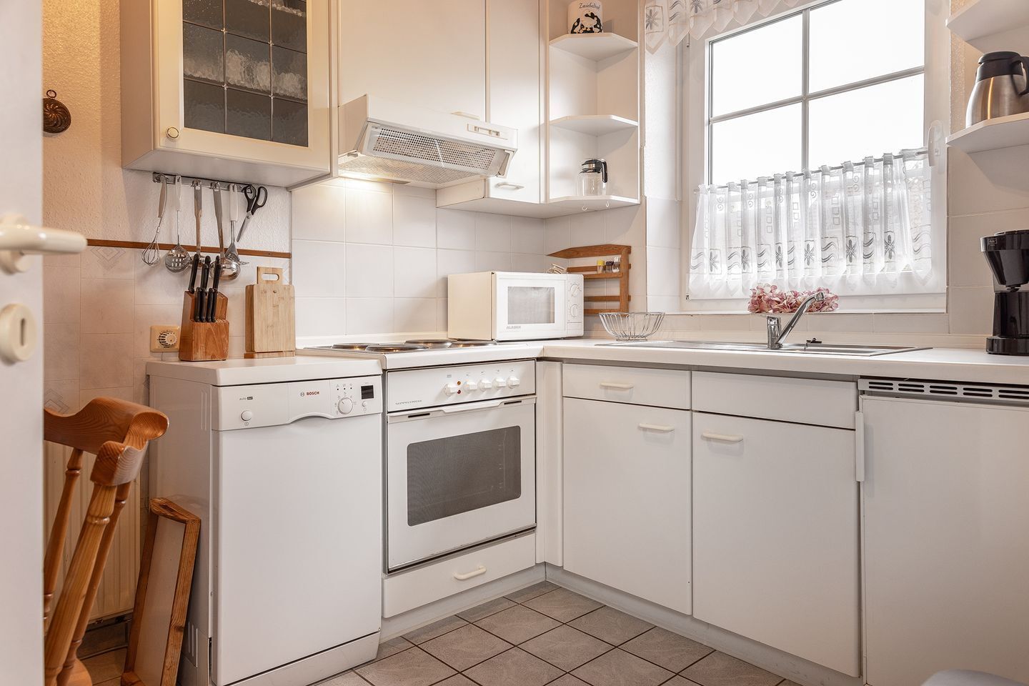 A compact kitchen with white cabinets, a Bosch stove, a microwave, and a window with curtains.