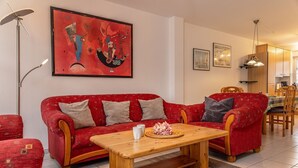 Een woonkamer met een rode bank, een houten bijzettafeltje en een schilderij aan de muur.