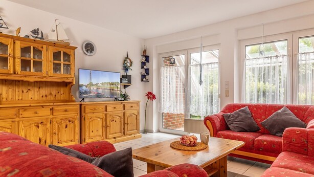 Een woonkamer met een houten kast, een rode bank, een televisie en een raam met gordijnen.