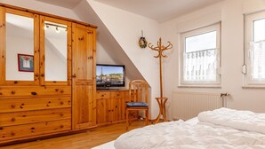 Een slaapkamer met een houten kast, een televisie, een stoel, een bed en een raam met gordijnen.