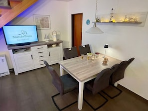 Eine moderne Küche mit Esstisch, Stühlen, einem Fernseher und einem Regal mit Dekoration.