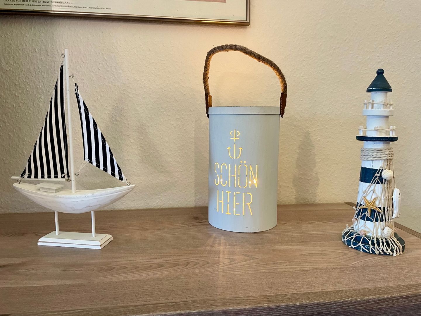 A wooden table with a small sailboat, a cylindrical container with text, and a lighthouse model.