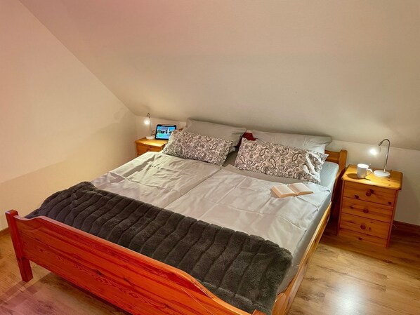 Une chambre à coucher avec un lit en bois, deux tables de chevet, une petite table, une lampe et un ordinateur portable posé sur l’une des tables.