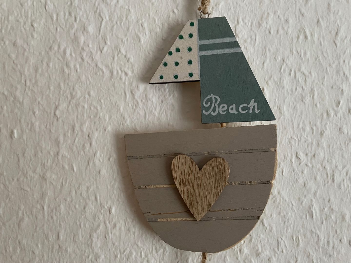 Een houten decoratie in strandthema met een hartvormige uitsparing en de tekst 'Beach'.