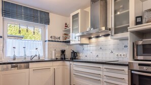 A modern kitchen with white cabinets, a stainless steel range hood, and a built-in microwave.