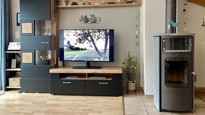 A modern living room with a flat-screen TV, wooden shelving, and a built-in wood stove.