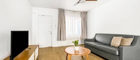 Una sala de estar moderna con un sofá gris, una mesa de centro de madera, un televisor de pantalla plana y un ventilador de techo.