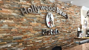 A reception desk with a stone wall background, a sign reading "Hollywood Beach Hotel", and a payment terminal. - Ocean's Sound Hotel (Hollywood)