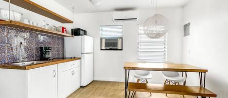 Een moderne keuken met witte kastjes, een houten aanrecht en een decoratieve spatwand. Er staat een eettafel met stoelen en een hanglamp.