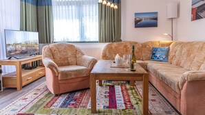 A cozy living room with a sofa, armchair, and coffee table. A television is on a wooden stand, and there is a window with curtains. - Vacation apartment 50036 - Comfortable and cozy: The vacation apartment is located in (Wittmund)