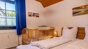 A bedroom with a crib, a bed, a nightstand with a lamp, and a window with blue curtains. - Vacation apartment 50036 - Comfortable and cozy: The vacation apartment is located in (Wittmund)