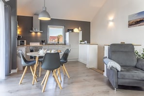 Et moderne køkken med spiseplads, en grå sofa og et stort vindue.