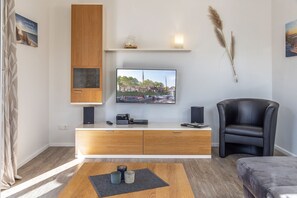 A modern living room with a flat-screen TV mounted on the wall, a wooden cabinet below, and a black leather chair. - 50047 Krabbenhaus House - Modern and comfortable: This stylish corner townhouse measuring approximately (Wittmund)
