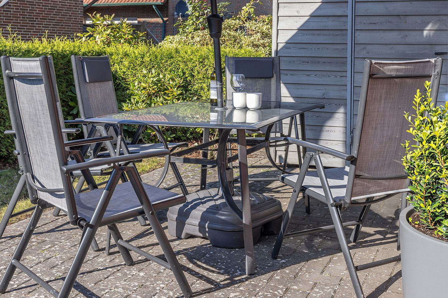An outdoor patio with a glass table, metal chairs, and a potted plant.