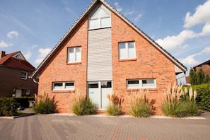 A two-story brick house with a central entrance, two windows on each side, and a sloped roof. - 50047 Krabbenhaus House - Modern and comfortable: This stylish corner townhouse measuring approximately (Wittmund)