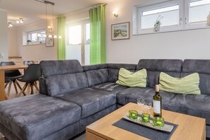 Un salon moderne avec un canapé d’angle gris, une table basse en bois et, au fond, un coin repas.