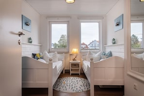 A room with two beds, a small table with a lamp, and a view of buildings outside. - 50111 Fisherman's Loft - Detached Vacation Home at the Friedrichsschleuse – (Wittmund)