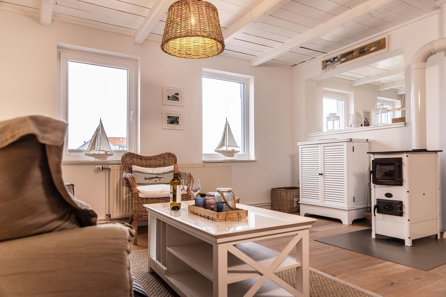 A cozy living room with a wicker chair, a table with a bottle and glasses, a white cabinet, and a fireplace.