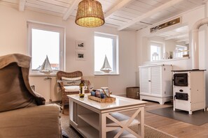 Un salon chaleureux avec un fauteuil en osier, une table avec une bouteille et des verres, un meuble blanc et une cheminée.