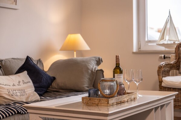 A cozy living room with a sofa, a lamp, a tray with a wine bottle and glasses, and a wicker chair.