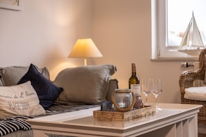 A cozy living room with a sofa, a lamp, a tray with a wine bottle and glasses, and a wicker chair. - 50111 Fisherman's Loft - Detached Vacation Home at the Friedrichsschleuse – (Wittmund)
