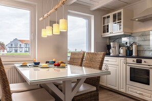 A modern kitchen with a glass dining table, wicker chairs, and pendant lights. - 50111 Fisherman's Loft - Detached Vacation Home at the Friedrichsschleuse – (Wittmund)