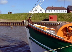En båt låg förtöjd vid en brygga, med en grönskande kulle och hus i bakgrunden.