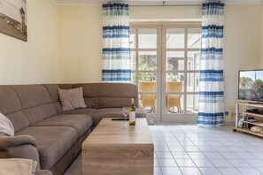 En stue med en brun sofa, et træbord, et fjernsyn og blåstribede gardiner.