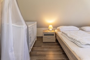 Et soveværelse med seng, natbord, lampe og en tremmeseng med hvid baldakin.
