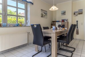 Uma sala de jantar com uma mesa de madeira, cadeiras pretas, um lustre e uma janela com vista para vegetação.