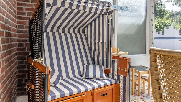 Une chaise à rayures avec un meuble en bois, une chaise en osier et une table donnant sur un mur de briques et une enseigne.