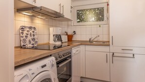 Cocina compacta con lavadora, cafetera y ventana sobre el fregadero.