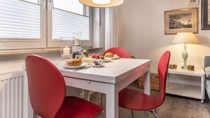 Un comedor con una mesa blanca, sillas rojas, una lámpara colgante roja, una vela y un cuadro en la pared.