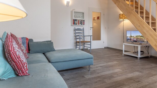 Una sala de estar moderna con un sofá gris, una escalera de madera y un televisor sobre un mueble.
