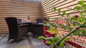 Un patio cubierto con una mesa, sillas, una botella de vino y una copa.