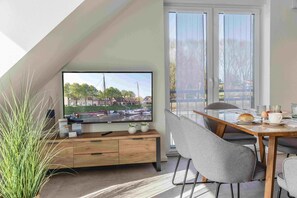 Un espace repas moderne doté d’un grand téléviseur, de meubles en bois et offrant une vue sur un canal où naviguent des bateaux.
