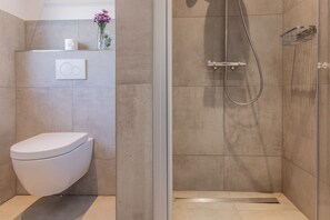 A modern bathroom with a toilet, a shower enclosure, and a shelf with toiletries.