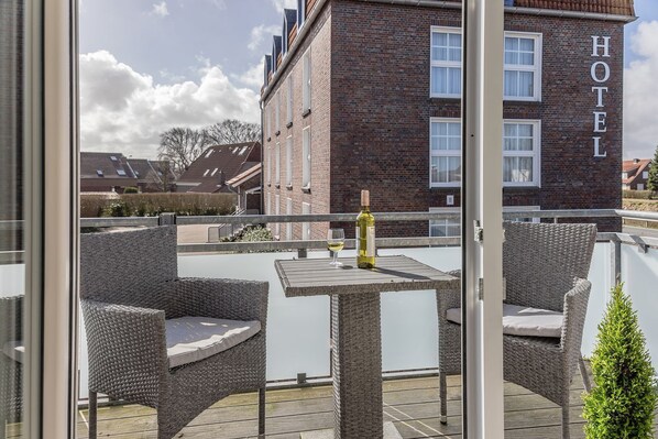 A rooftop terrace with wicker furniture, a bottle of wine, and a view of a hotel building in the background.