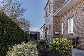 Un bâtiment en briques avec un toit plat, une porte de garage bien visible et une haie bien entretenue.