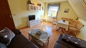 A cozy living room with a sofa, a coffee table, a TV, and a dining area with a table and chairs. - Diedrich - Holiday apartment Diedrich (Wyk auf Föhr)