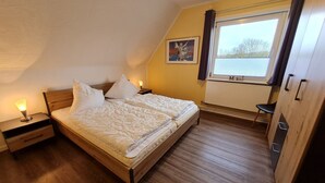 A bedroom with a wooden bed, a nightstand, a window with curtains, and a radiator. - Diedrich - Holiday apartment Diedrich (Wyk auf Föhr)