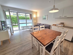 Une cuisine moderne avec des meubles blancs, une table à manger en bois et un four encastré.