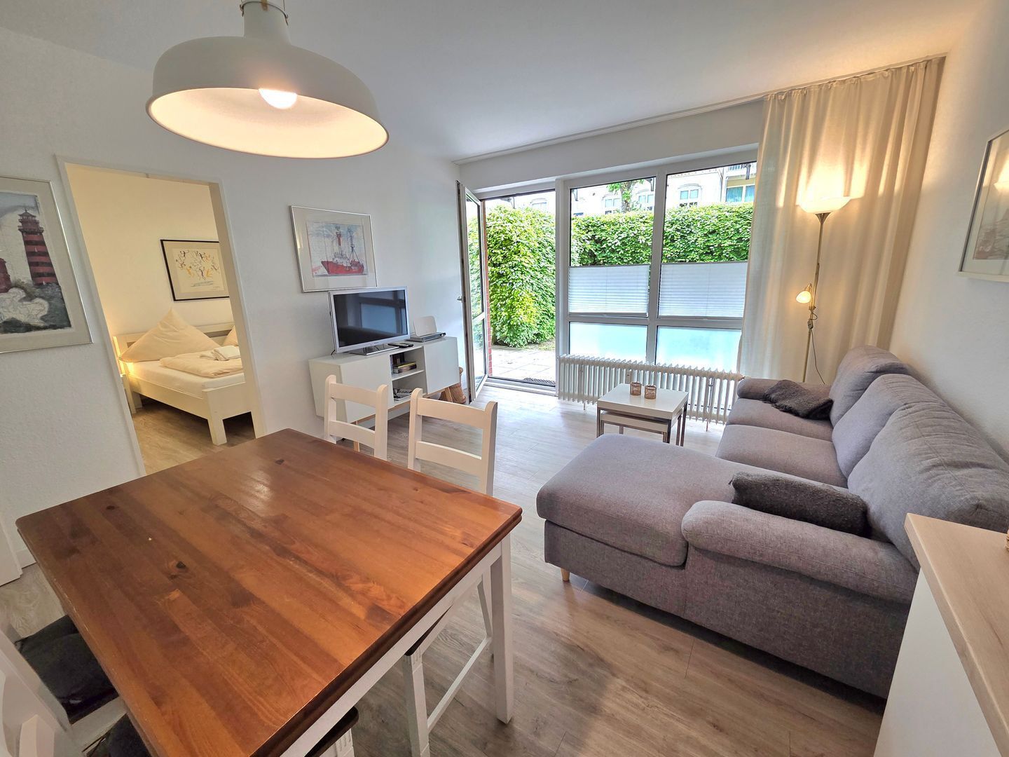 Una sala de estar moderna con una mesa de comedor de madera, un sofá gris y un televisor sobre un mueble blanco.