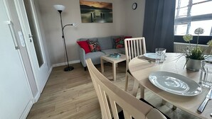 Una sala de estar moderna con comedor, que incluye un sofá, una mesa de centro, una lámpara de pie y un cuadro en la pared.