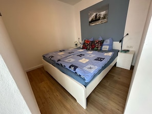 A bedroom with a bed, a nightstand, a lamp, and a painting on the wall.