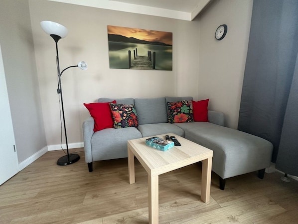 A modern living room with a grey sofa, a wooden coffee table, a floor lamp, and a painting of a sunset over water.