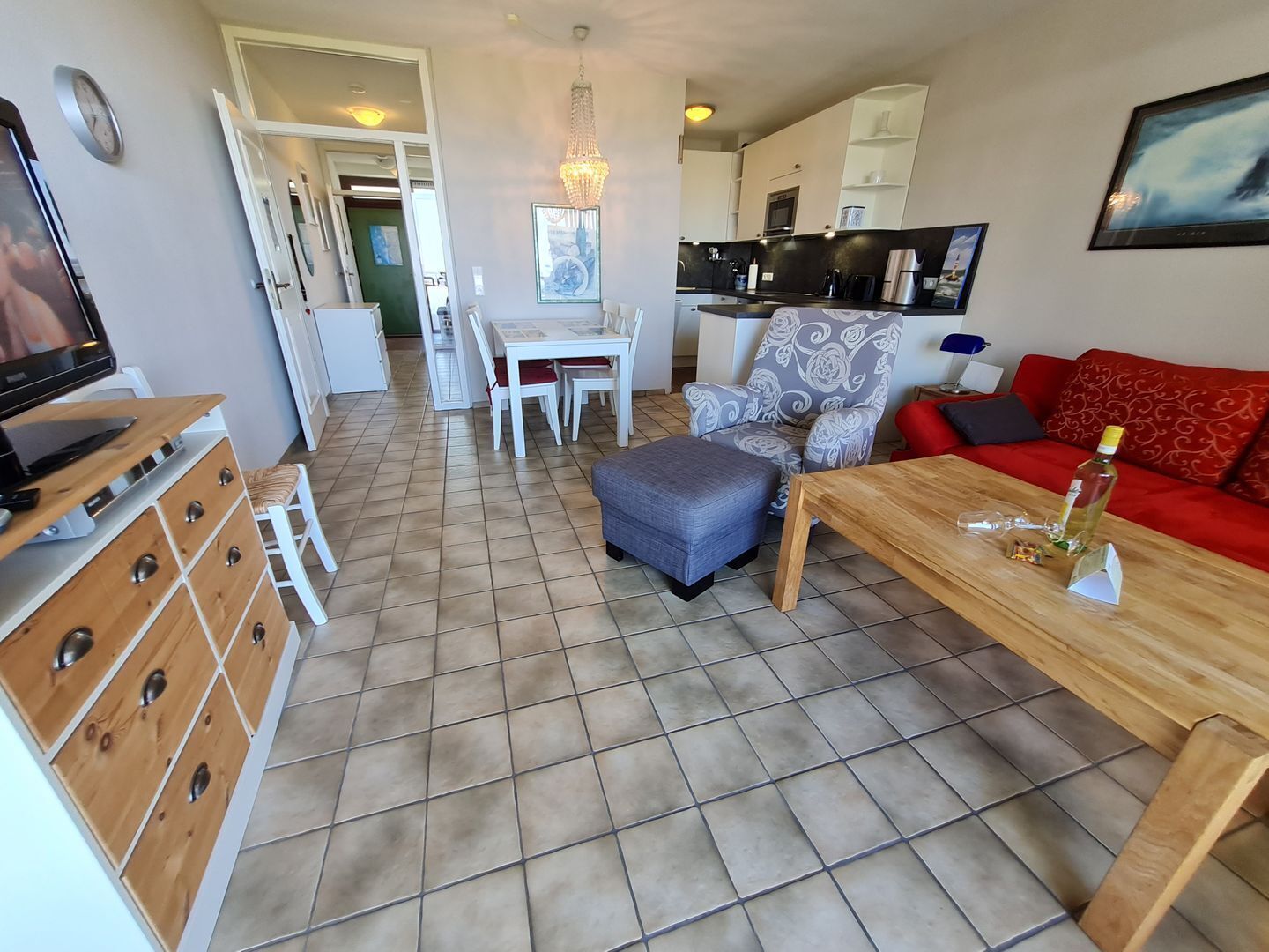Ein Wohnzimmer mit Fernseher, Holzmöbeln, einem roten Sofa und einer Essecke mit Tisch und Stühlen.