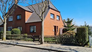 A two-story brick house with a sloped roof, a wooden fence, and a tree in the foreground. - Am Museum - Holiday cottage Am Museum (Wyk auf Föhr)