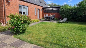 A brick house with a satellite dish, a patio with a table and chairs, and a well-maintained lawn. - Am Museum - Holiday cottage Am Museum (Wyk auf Föhr)