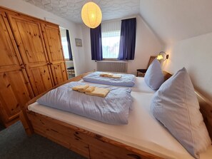 Quarto com duas camas, guarda-roupa de madeira e luminária pendente.
